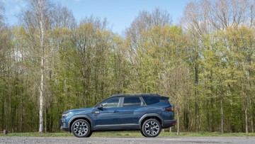 Dacia Bigster Hybrid 155 stehend auf einem Parkplatz mit blühenden Birken im Hintergrund